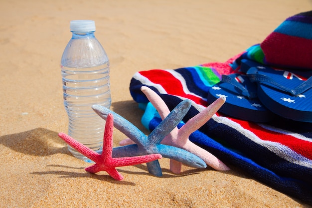 Beach towel and bottle of cool water on sandy beach