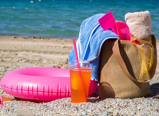 A beach towel is next to a pink bag with a pink straw.