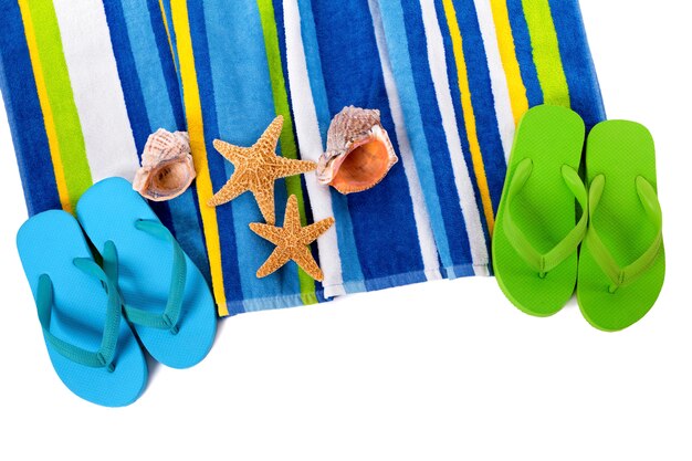 Beach towel with flip flops, starfish and seashells isolated on white.