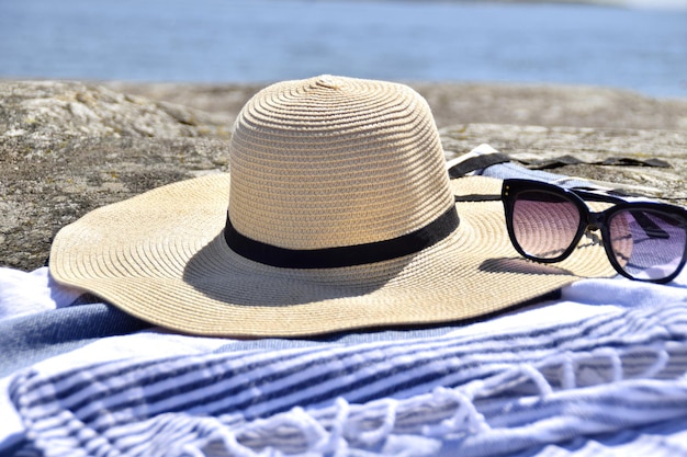 A beach towel a women's straw hat and sunglasses lie on the shore