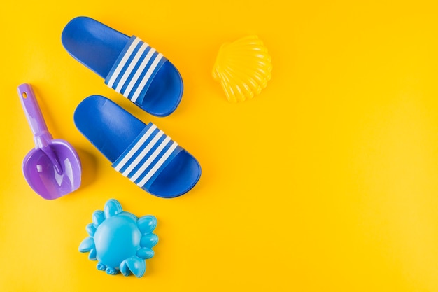 Beach toys and blue flip flops on yellow background