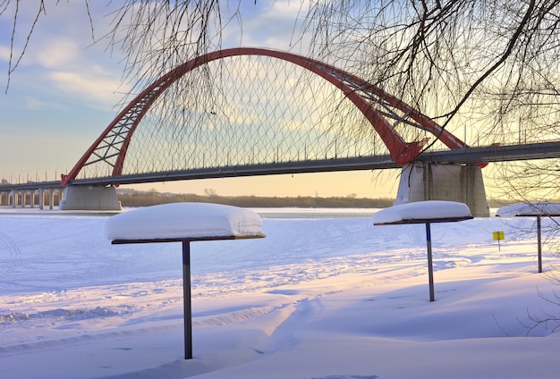 Beach umbrellas covered with snow under the arch of the Bugrinsky automobile bridge on the bank