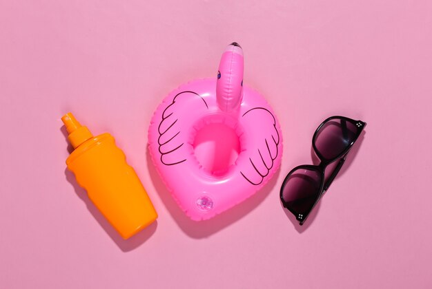 Beach vacation. Inflatable flamingo and sunblock bottle, sunglasses on bright pink