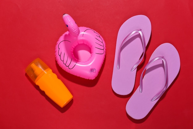 Beach vacation. Inflatable flamingo and sunblock, flip flops on bright red.