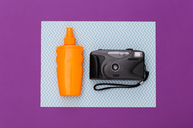 Beach vacation, travel concept. Sunblock bottle and camera on purple blue