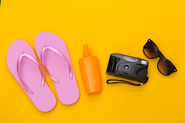 Beach vacation, travel concept. Sunblock bottle, sunglasses, flip flops and camera on yellow