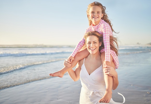 Passeggiata sulla spiaggia bambino sorriso e madre che trasportano bambino in vacanza via mare in australia durante l'estate viaggio in famiglia ritratto di ragazza e mamma che giocano con le spalle in vacanza nella natura per rilassarsi con il mockup