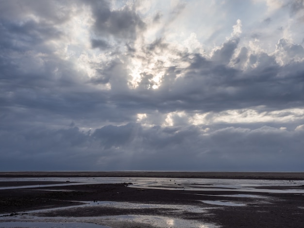 Foto spiaggia con un sole splendente che splende tra le nuvole all'ora del tramonto