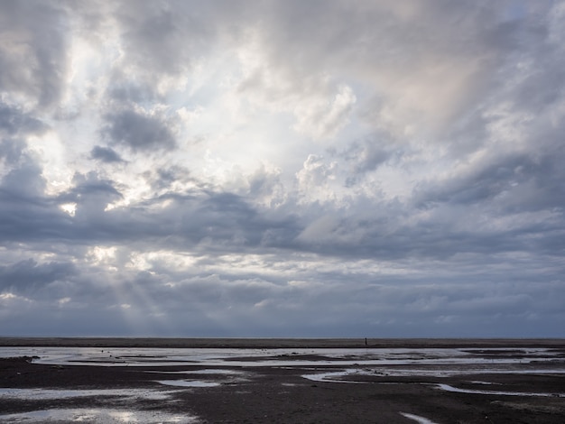 Foto spiaggia con un sole splendente che splende tra le nuvole all'ora del tramonto