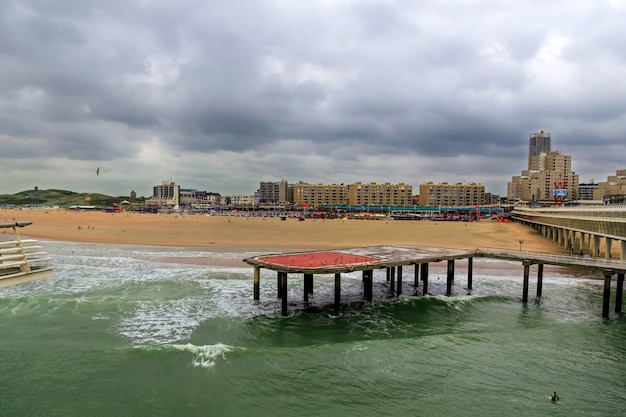 A beach with a pier in the foreground and a building in the background.