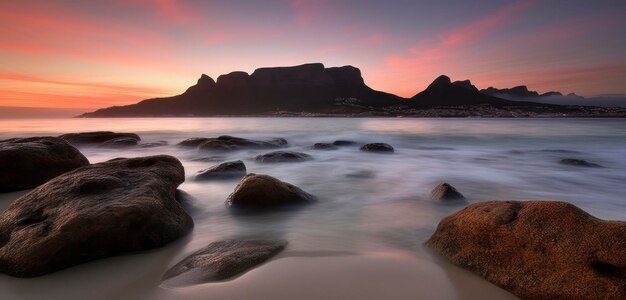 A beach with rocks and a pink sky in the background