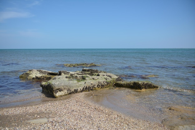Пляж со скалами и водой на переднем плане и морем на заднем плане.