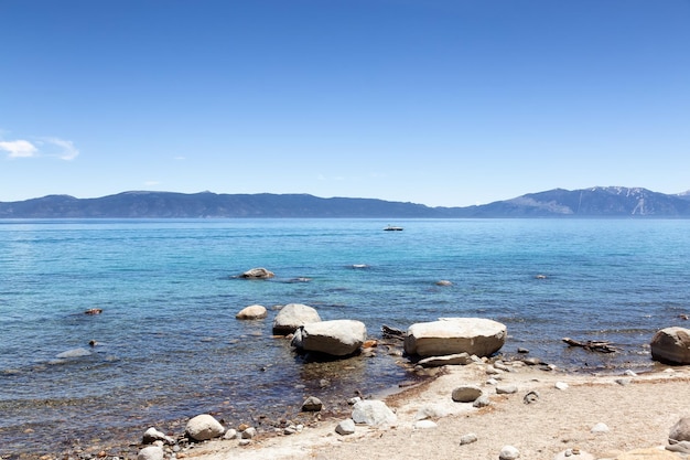 Beach with sand and rocks at lake surrounded by mountains summer season