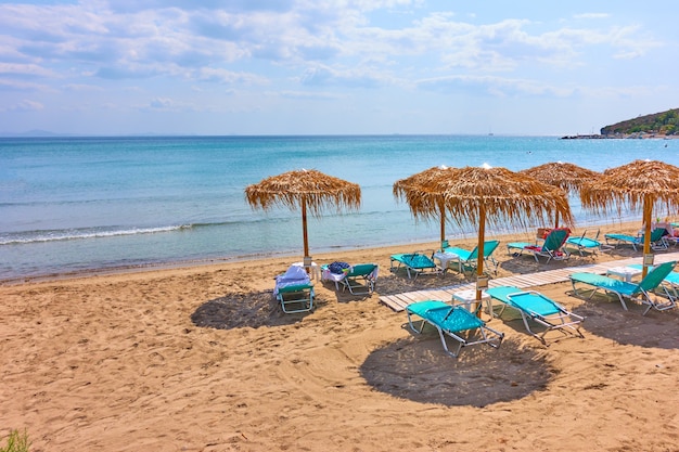 Photo beach with straw umbrellas by the sea on sunny summer day, agia marina, aegina island, greece - greek resort