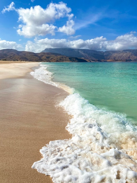 Foto spiaggia con onde turchesi sullo sfondo di montagne e cielo azzurro bellissimo sfondo del mare