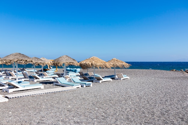 Beach with umbrellas and deck chairs by the sea in Santorini