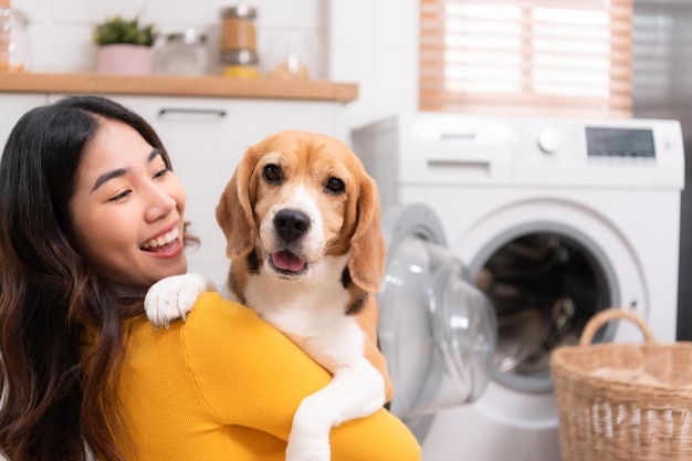 母親が洗濯機に服を入れている間、飼い主の腕の中でカメラを見つめるビーグル犬