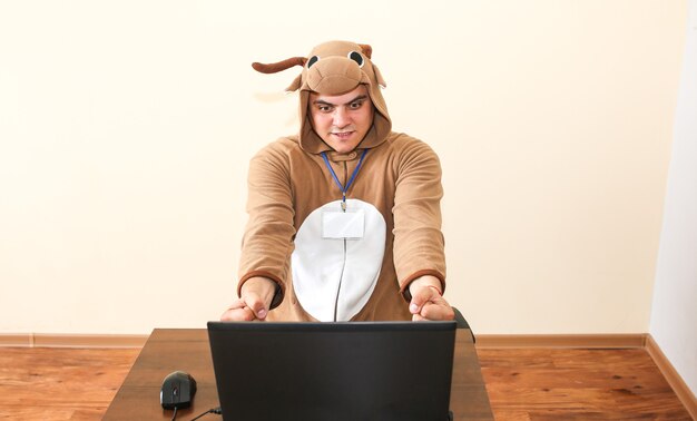 Beambte in cosplay kostuum van een koe. Kerel in de grappige dierenpyjama's nachtkleding in de buurt van de laptop. Parodie op wanhopige manager. Beroepsmatige burn-out.