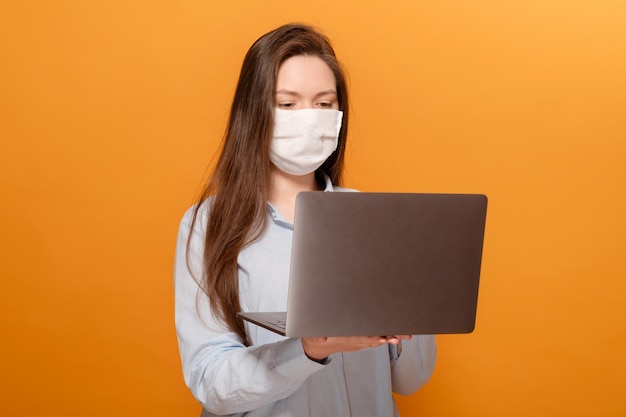 Beambte met in hand laptop en een medisch masker op gezicht op geeloranje freelancer achtergrond ,.