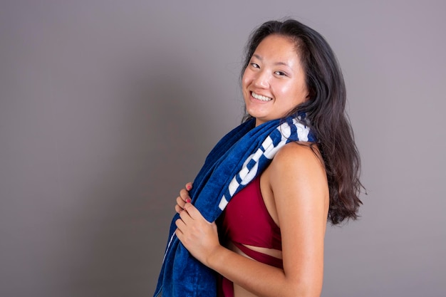A beaming Asian woman with a blue towel postworkout