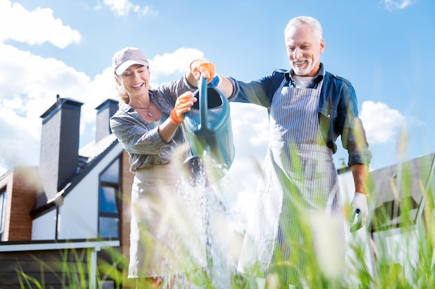 Beaming couple. Beaming loving couple holding big garden sprinkler while watering plants in garden bed together