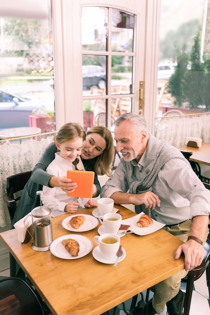 Photo beaming grandparents. happy beaming grandparents eating morning croissants with cute little granddaughter