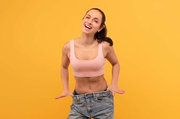 a beaming young woman confidently pulls at her oversized denim jeans to showcase her successful