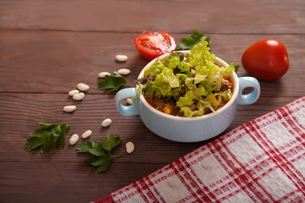 木製のテーブルに豆のスープ、トマト、豆、パセリ、市松模様のリネンナプキン。
