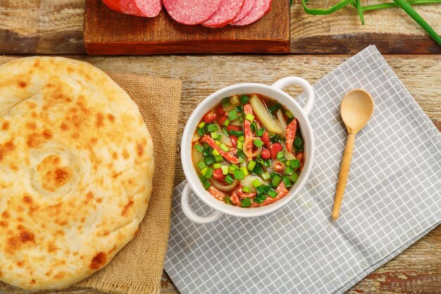 Bean soup with smoked Jewish cuisine cholit in a tureen on a gray napkin next to a sausage