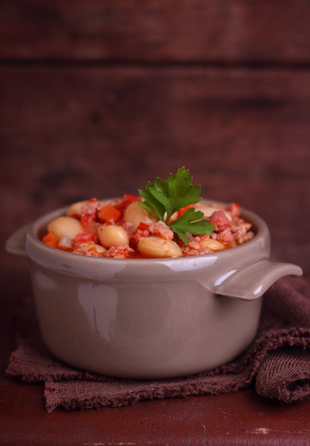 Bean stew with meat and vegetables on a dark wooden background