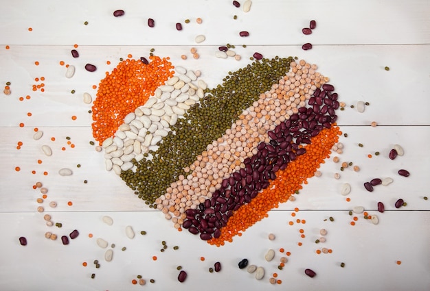 Photo beans, lentils and beans laid out in the form of a heart on a white wooden background