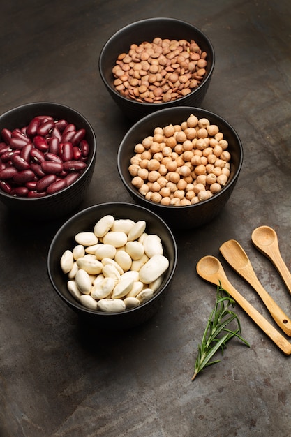 Photo beans lentils and chickpeas in black bowls with wooden spoons on a rusty table