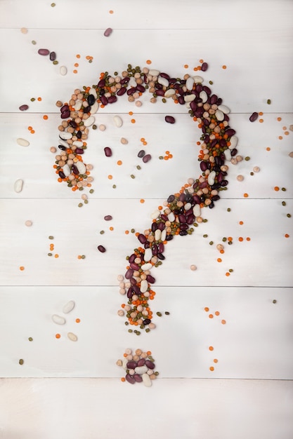 Beans, lentils, peas laid out on a white wooden background in the form of a question mark