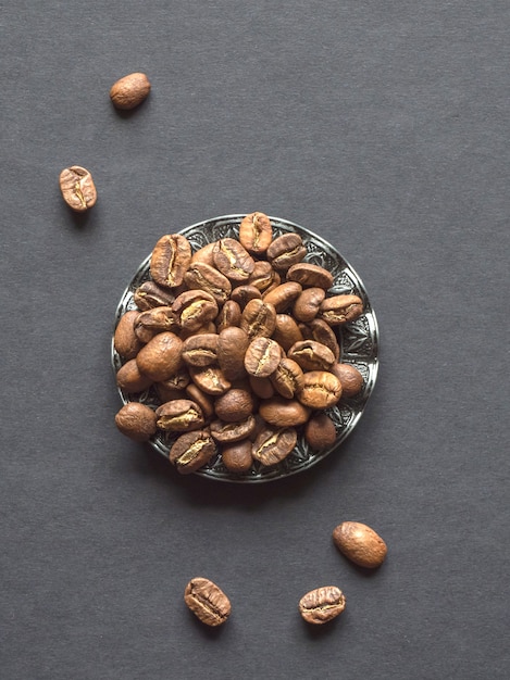 Beans of roasted coffee in a vintage plate on a black table.