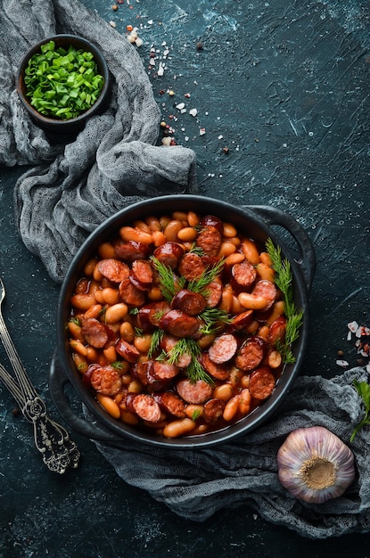 Beans with sausages in tomato sauce on a black plate.  Top view. Free space for your text.