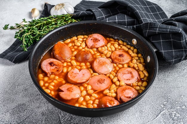 Beans with sausages in tomato sauce in a pan.