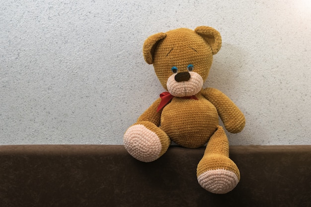 A bear sitting alone on the back of the sofa. Beautiful knitted toy.