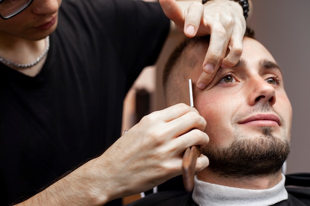 Beard haircut in a barbershop, a young guy shaving his beard with a razor, close-up