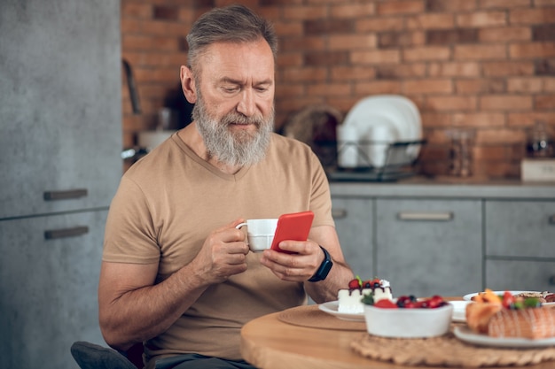 A bearded amn sitting at the table in the kitchen and looking contented