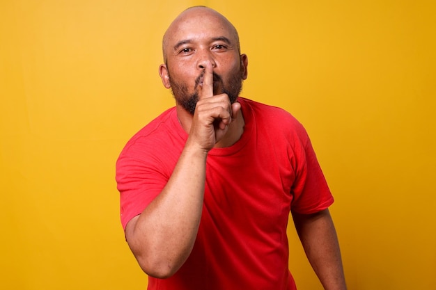 Bearded bald man keeps finger on lips asks not tell secret information or keep silence