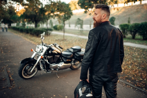 Bearded biker with helmet in hand goes to his chopper