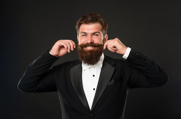 Bearded bridegroom in tuxedo on black background, menswear