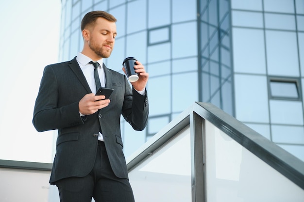 Bearded businessman in formal suit on break using mobile phone use smartphone business man standing outside on modern urban city street background with coffee cup in downtown outdoors copy space