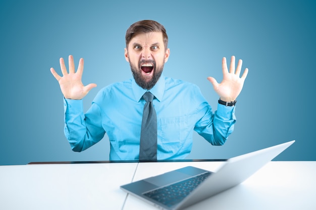 A bearded businessman behind a laptop holds out his hands and shouts, a man in a blue shirt shows the emotions of the scream