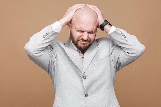 Bearded businessman in light gray suit standing and holding his painful head