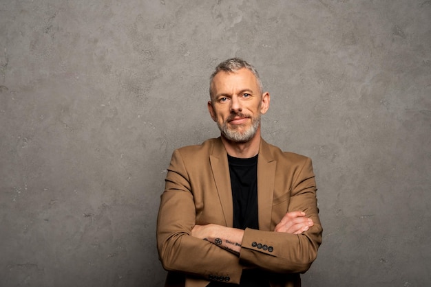 Bearded businessman standing with crossed arms and looking at camera on grey