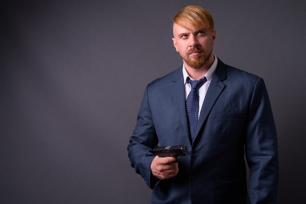 Bearded businessman with handgun on gray