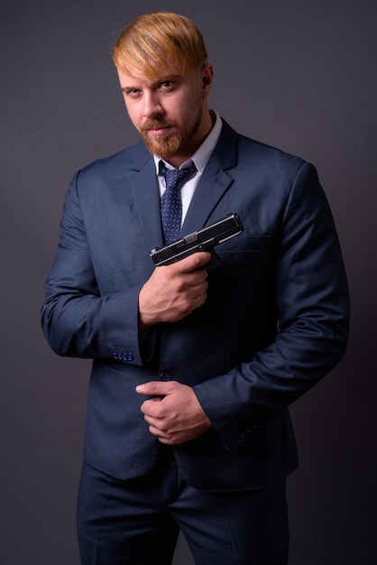 Bearded businessman with handgun on gray