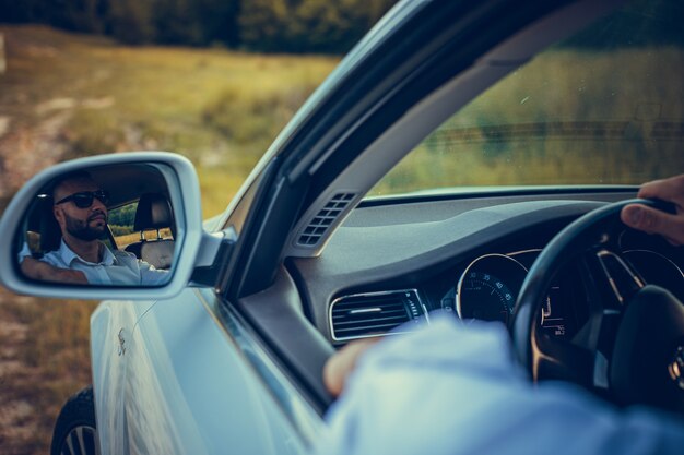 Bearded caucasian business man looking at camera through rear\
view mirror head and shoulders