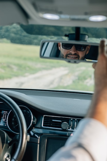 Bearded caucasian business man looking at camera through rear\
view mirror. summer background.